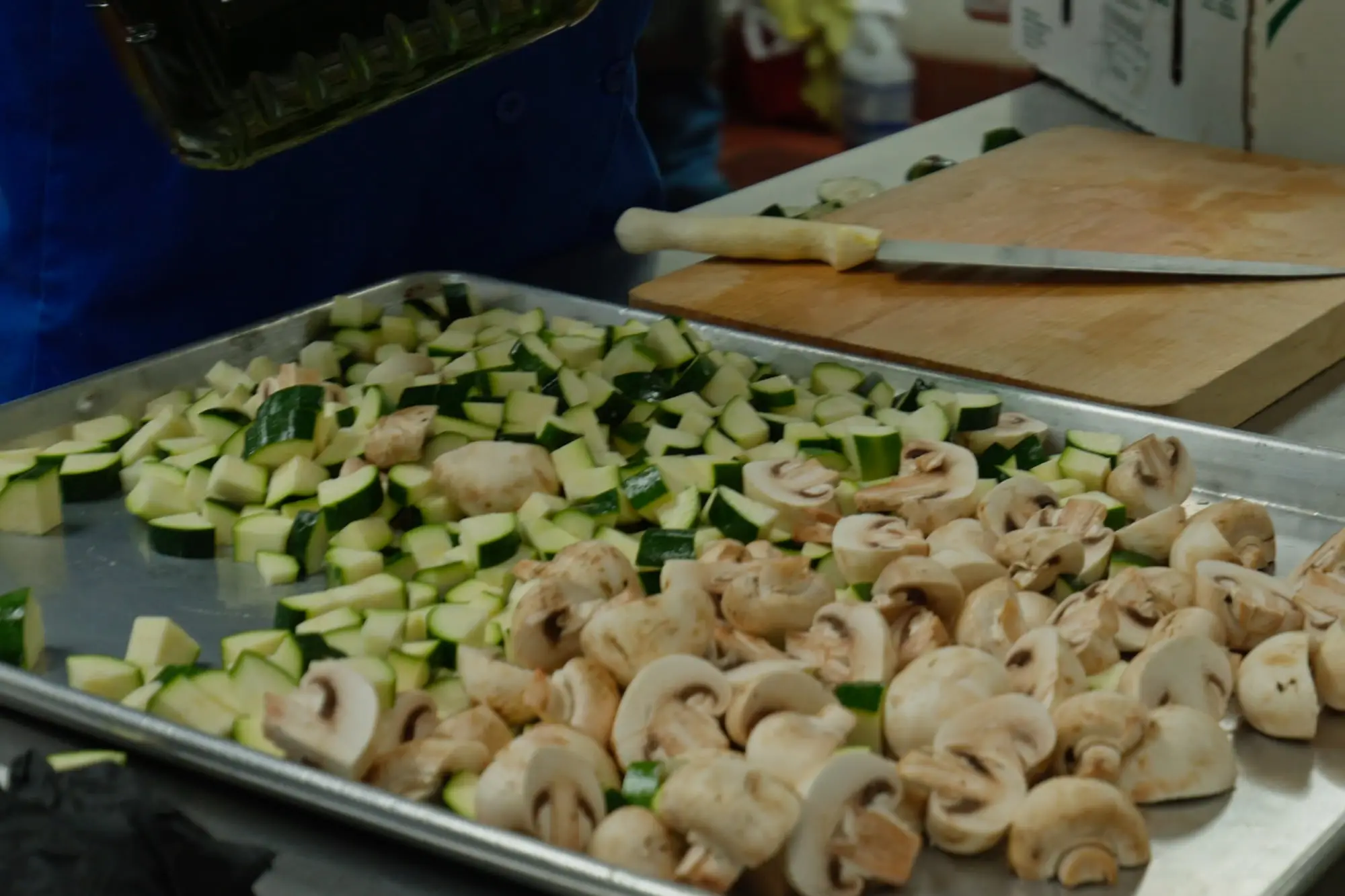 Sheet pans of fresh zucchini and mushrooms prepped for a catering order
